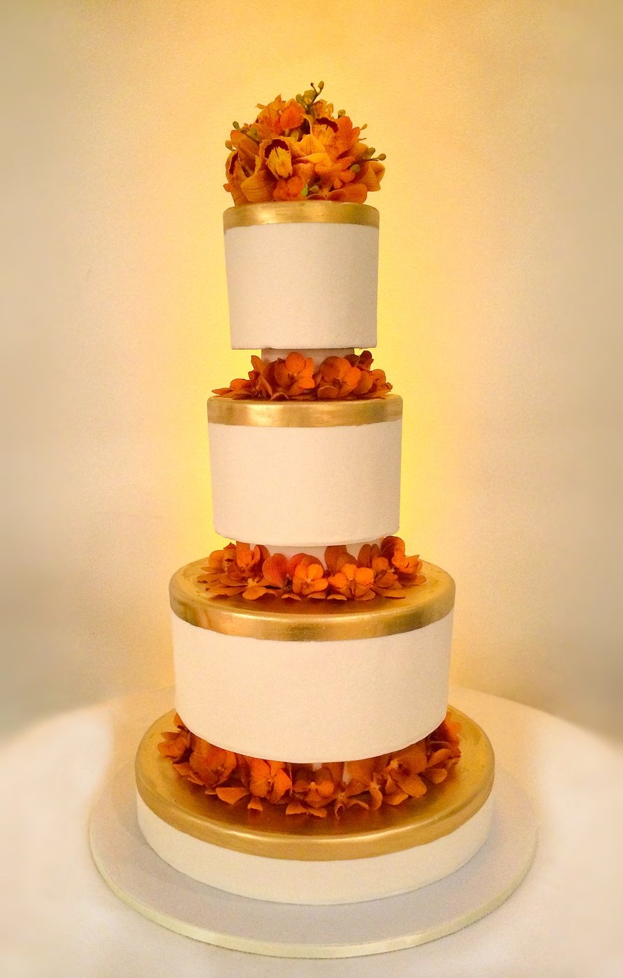 Tiered white and gold cake with orange flowers